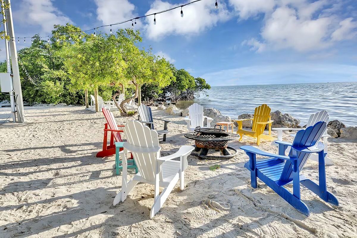 Adirondack chairs around a firepit on the private beach at this Key Largo vacation home
